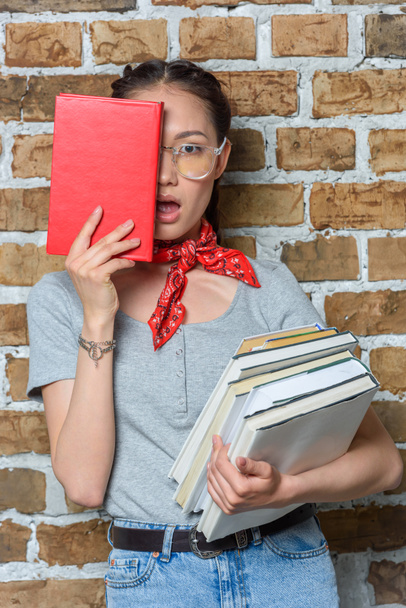 elegante chica asiática sosteniendo libros con expresión facial
 - Foto, imagen