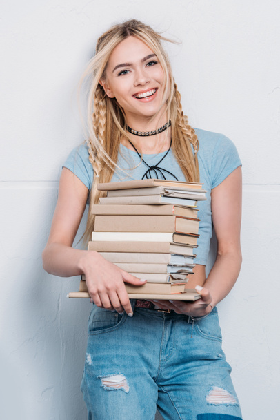 joven sonriente mujer caucásica sosteniendo libros y mirando a la cámara
 - Foto, Imagen