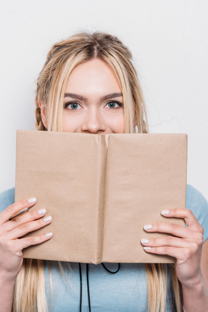 jeune femme blonde tenant livre devant le visage et regardant la caméra
 - Photo, image