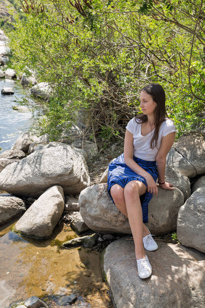 Όμορφη κοπέλα που κάθεται πάνω σε ένα βράχο στην όχθη - Φωτογραφία, εικόνα