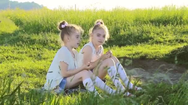 Dvě malé holčičky sedící na trávě mluví bavit - Záběry, video