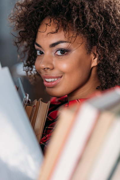 Atractivo joven afroamericano estudiante sosteniendo libros y sonriendo a la cámara
  - Foto, Imagen