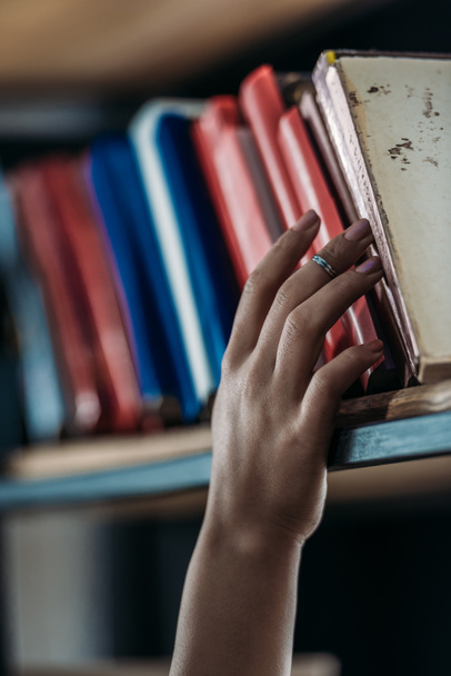 Schnappschuss von Studentin, die Buch im Bücherregal in Bibliothek hält   - Foto, Bild