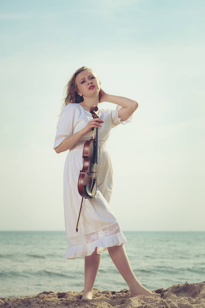 Woman on beach near sea holding violin - Foto, afbeelding