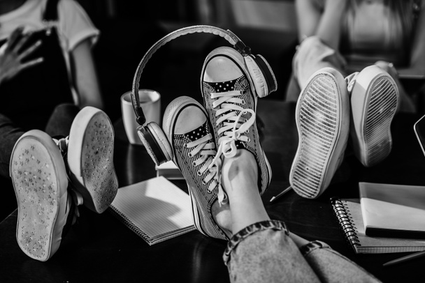 Γκρο πλαν θέα πόδια της γυναίκας στα κομψά παπούτσια με ακουστικά στο ξύλινο τραπέζι, μαύρο και άσπρο φωτογραφία - Φωτογραφία, εικόνα