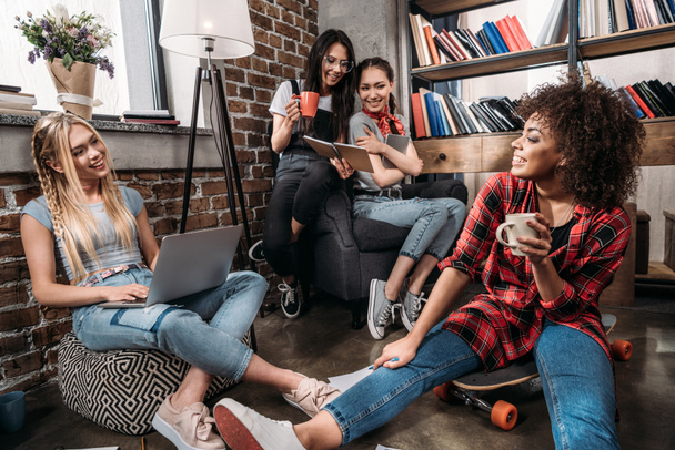 Uśmiechający się młodych kobiet siedząc razem z laptopa i filiżanki do kawy, studiowania i mówienie w pomieszczeniu - Zdjęcie, obraz
