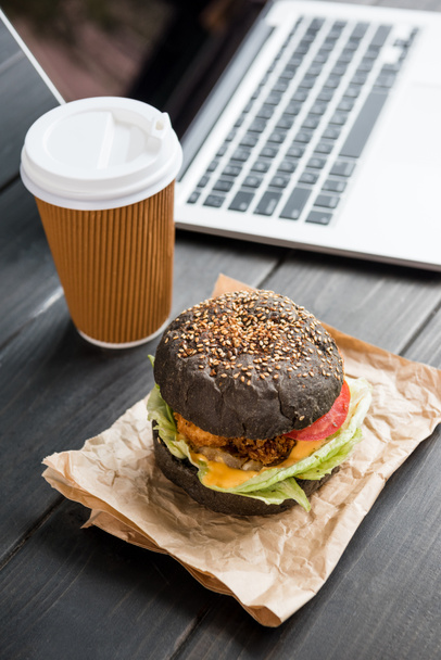 close up of burger with coffee to go and laptop on wooden tabletop - Zdjęcie, obraz