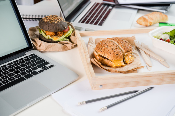 テーブルの上のノート パソコンとサラダとパンの新鮮なパンとおいしいハンバーガー - 写真・画像