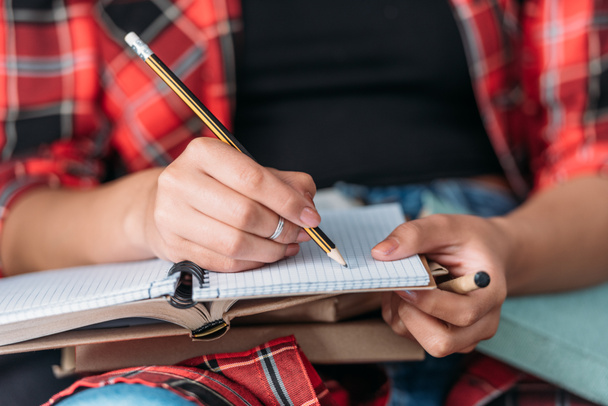 Schnappschuss eines Studenten, der Bücher hält und mit Bleistift in ein Notizbuch schreibt - Foto, Bild
