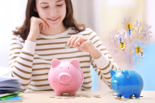 Young smiling girl putting coins into piggy bank. Saving for education concept - Foto, Bild
