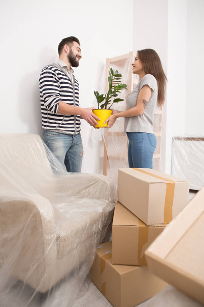 Moving in, happy male and female unpacking boxes, holding plant. - Foto, afbeelding