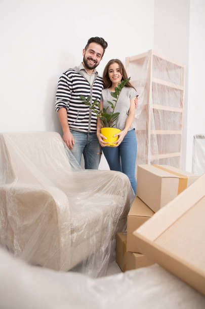 Μετεγκατάσταση, yong ζευγάρι που στέκεται στο νέο διαμέρισμα με έπιπλα coverd με αλουμινόχαρτο. - Φωτογραφία, εικόνα