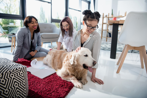 Multiethnische Geschäftsfrauen streicheln Hund im Büro - Foto, Bild