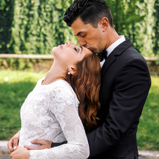 Bride throws her head back and groom kisses her forehead - Zdjęcie, obraz