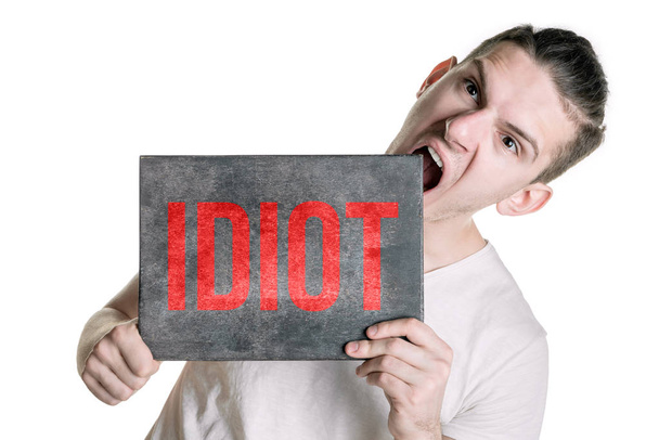 Een jonge man in een T-shirt met een spandoek met het opschrift "idiot" probeert te bijten de banner. Horizontale frame - Foto, afbeelding