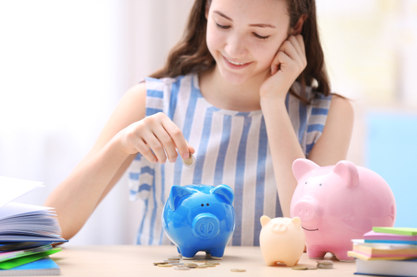 Young smiling girl putting coins into piggy bank on light background. Saving for education concept - Foto, Bild