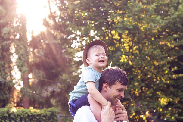 Vater und Sohn gehen bei Sonnenuntergang spazieren. glücklicher Vater und kleiner Sohn in der Sonne. - Foto, Bild