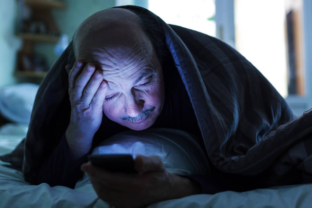 Un anciano intenta conciliar el sueño y revisa el correo o las llamadas
 - Foto, imagen