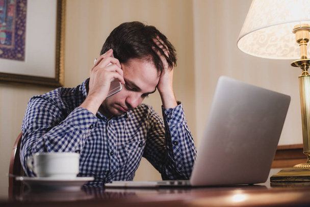 zmęczony człowiek z laptopa i kawy po pracy zadzwonić na swój telefon, biznesmen, w biurze lub w domu - Zdjęcie, obraz
