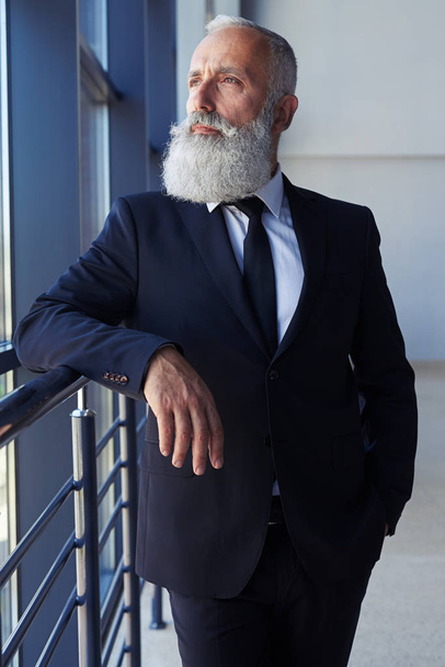 Задумчивый человек с седой бородой смотрит в окно
 - Фото, изображение