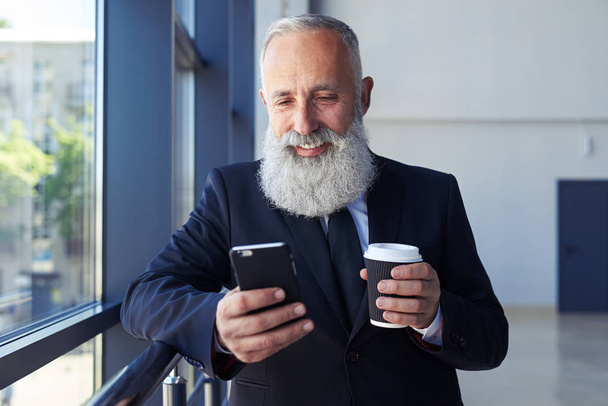 Solider Mann hält Tasse Kaffee in der Hand und surft im Telefon - Foto, Bild