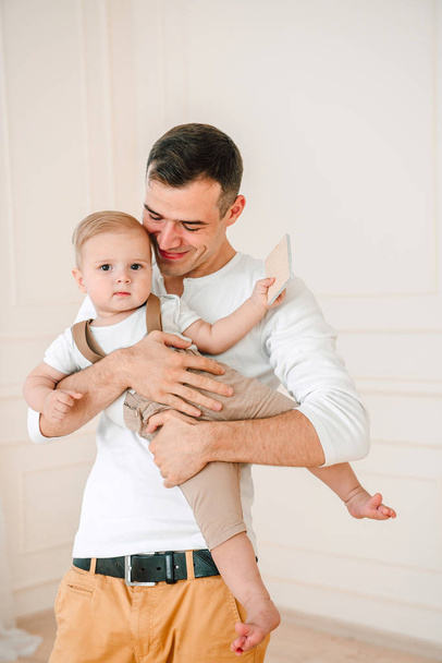Portret przystojny ojciec i syn 1 rok stary zabawy szczęśliwa i uśmiechnięta, przytulanie w studio w czasie dnia. Pojęcie przyjazny rodzinie. - Zdjęcie, obraz
