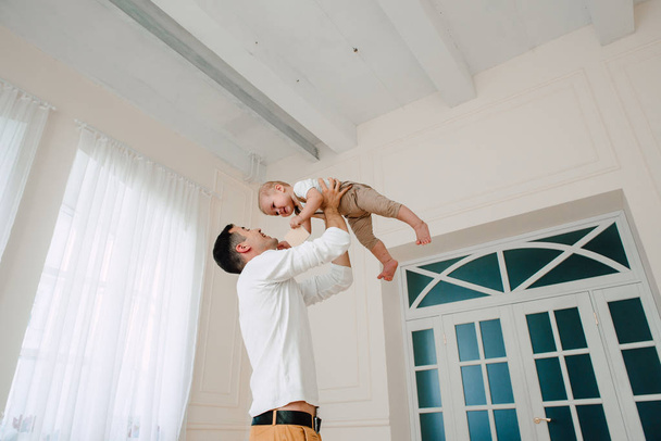 Porträt eines gut aussehenden Vaters und eines einjährigen Sohnes, die sich am Tag glücklich und lächelnd im Studio umarmen. Konzept der freundlichen Familie. - Foto, Bild