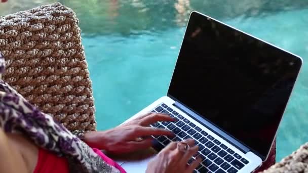Женщина, работающая за ноутбуком, сидит в кресле у бассейна на острове Бали
. - Кадры, видео