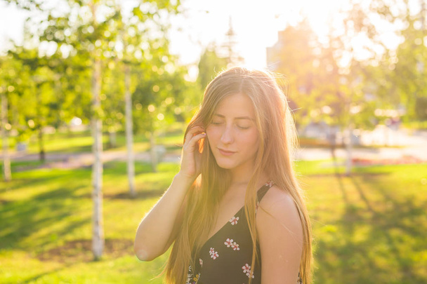 Aantrekkelijke jonge vrouw genieten van haar tijd buiten in park met zonsondergang in de achtergrond - Foto, afbeelding
