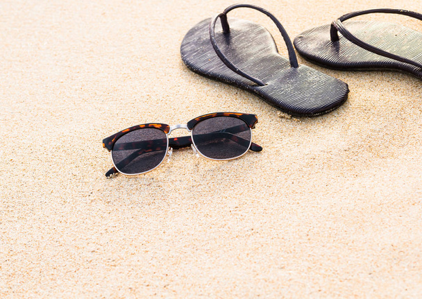 zonnebrillen en donker paarse slippers op gereinigde zand op strand, zomer - Foto, afbeelding