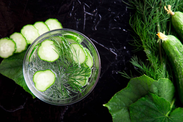 Cucumber water in glass with dill on black background. Detox, diet. Backlight. Top view. Copy space. - Photo, Image