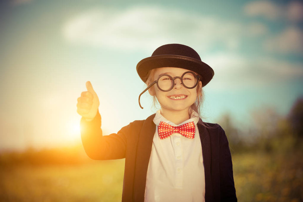 Funny little girl in bow tie and bowler hat showing thumb up. - Photo, image