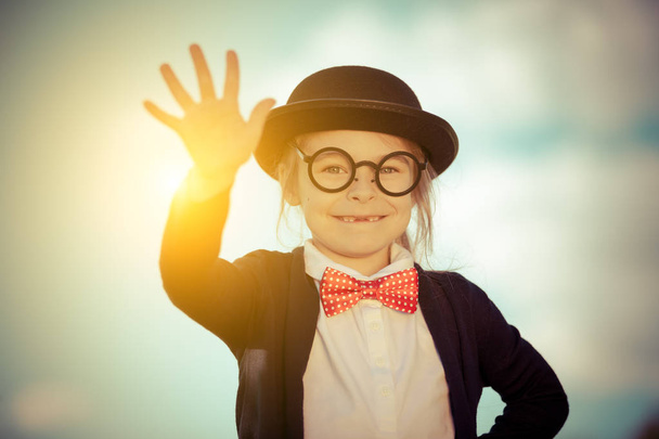 Funny little girl in bow tie and bowler hat with hello gesture. - 写真・画像