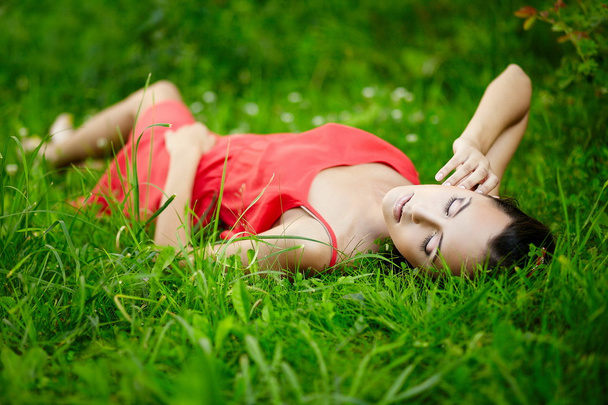 Girl lying in green summer bright grass in the park in red dress - Fotografie, Obrázek