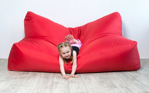 大きな赤いソファの上に横たわる幼児の女の子 - 写真・画像