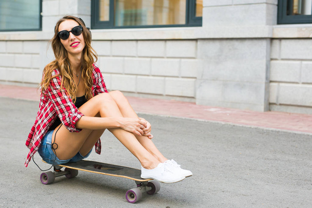 Piękna młoda kobieta w okulary siedzenia na skate, lifestyle moda ulicy. - Zdjęcie, obraz