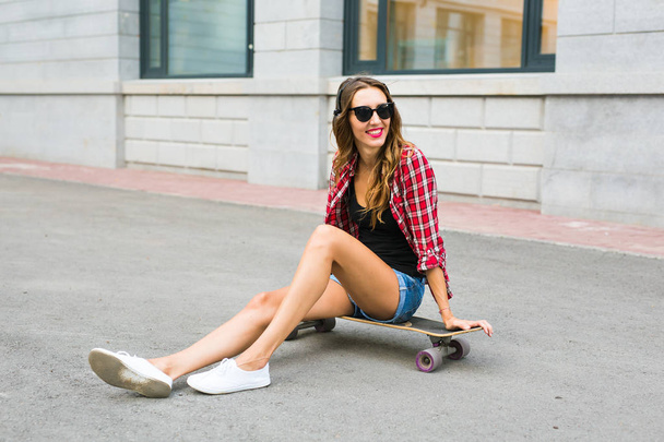 Piękna młoda kobieta w okulary siedzenia na skate, lifestyle moda ulicy. - Zdjęcie, obraz