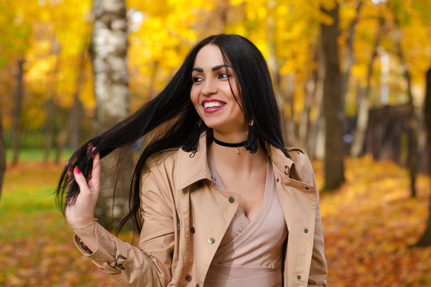 charming smiling brunette on background of autumn park - Фото, изображение