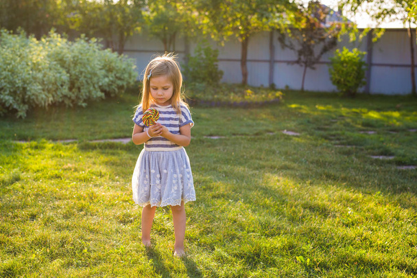 cute little girl eating a lollipop on the grass in summertime. - Photo, image