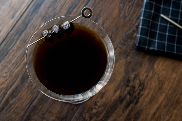 Black Manhattan Cocktail with olives on dark wooden surface. - 写真・画像