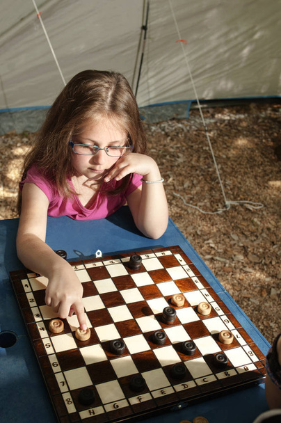 Mała dziewczynka gra warcaby pokładzie odkryty (camping) w słoneczny letni dzień.  - Zdjęcie, obraz