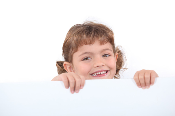 Little blonde girl laughing is half hidden behind a white panel - Foto, Imagen
