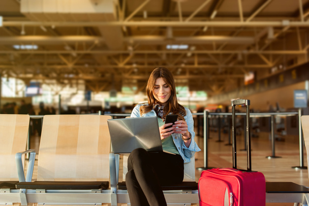 Жінка-пасажир на смартфоні та ноутбуці сидить у термінальному залі
 - Фото, зображення