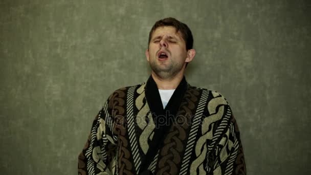A man in a dressing gown sneezes at home. A man is sick, sneezes and coughs. - Footage, Video
