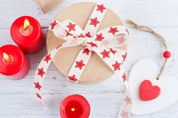 Gift in kraft box with red stars ribbon, lit candles and heart - Photo, Image