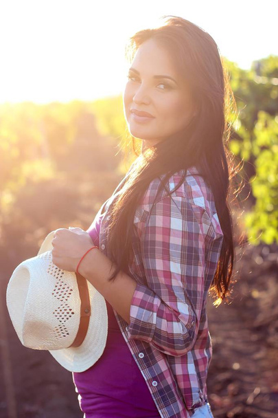 Mladá krásná žena chodí ve vinicích. Portrét krásné mladé ženy s kloboukem v letních paprscích slunce. Šťastná mladá žena se těší letní západ slunce na vinici. - Fotografie, Obrázek