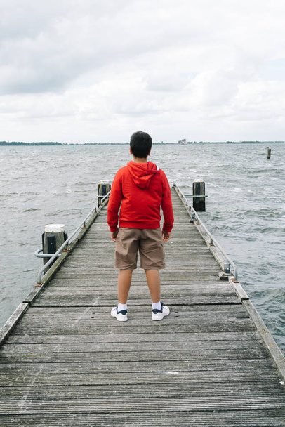 Rückansicht eines Jungen mit lässiger Kleidung auf einem hölzernen Pier - Foto, Bild