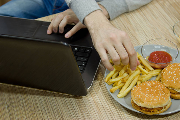 A man works at a computer and eats fast food. unhealthy food: Bu - Foto, afbeelding