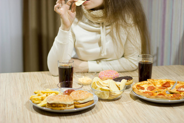 The girl is sitting at the table and eating fast food.  - Фото, зображення