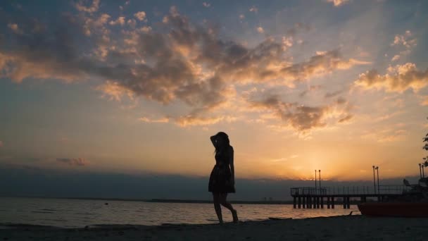 Portret van een aantrekkelijk meisje blootsvoets lopen op het zand op het strand bij zonsondergang. Silhouet van een mooi meisje op de oever van de Oceaan. Slow motion - Video